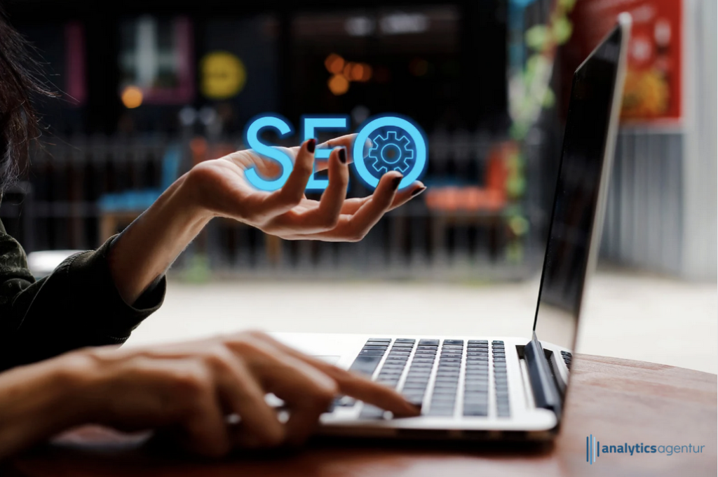 Eine Hand hält ein leuchtendes SEO-Symbol über einem Laptop, während die andere Hand auf der Tastatur tippt.